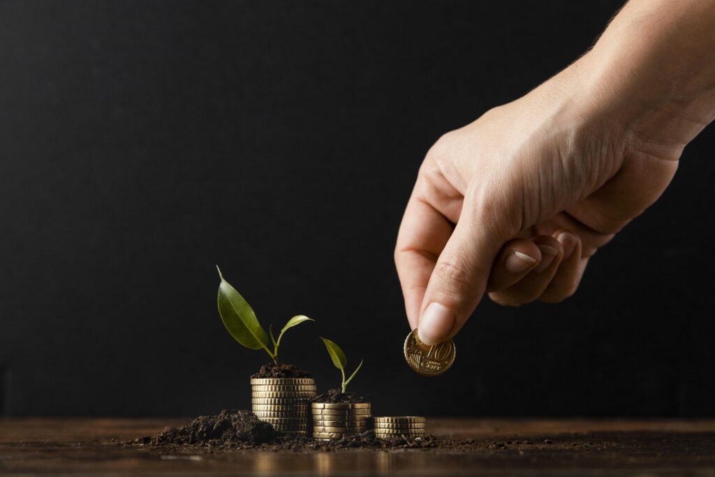 A hand planting a coin in soil with small plants growing from stacked coins, symbolizing financial growth and investment